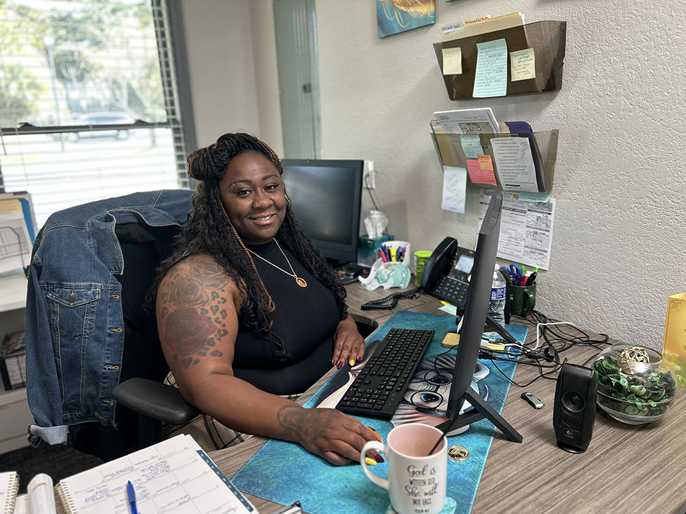 LeKita, seated at her desk in a multifamily complex in Charleston, SC, where she both lives and works. She is focused and professional, surrounded by office equipment and paperwork.